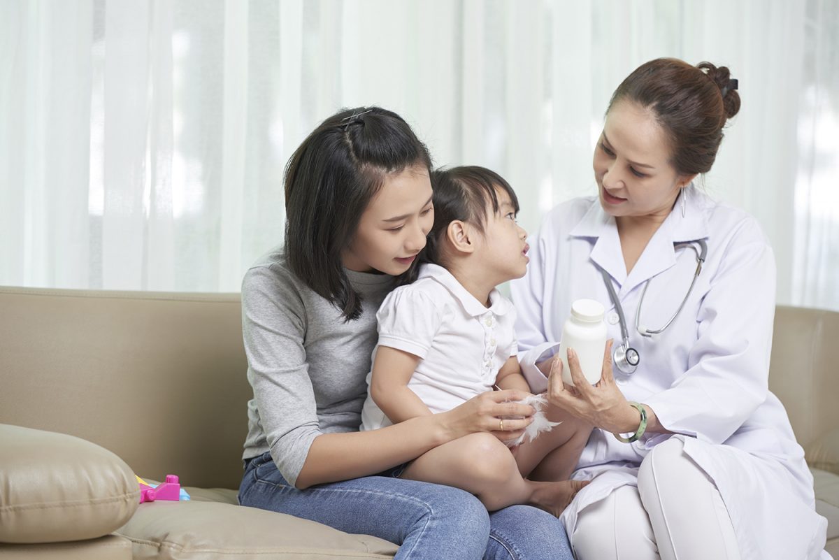 แพทย์เวชศาสตร์ครอบครัว พูดคุยและตรวจอาการเด็กเล็กที่นั่งอยู่บนตักแม่ของเด็กอย่างอบอุ่นใกล้ชิด