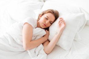ผู้หญิงวัยรุ่นกำลังนอนหลับอย่างสบายในท่านอนตะแคงที่ถูกต้อง หมอนและที่นอนรองรับสรีระได้ดี